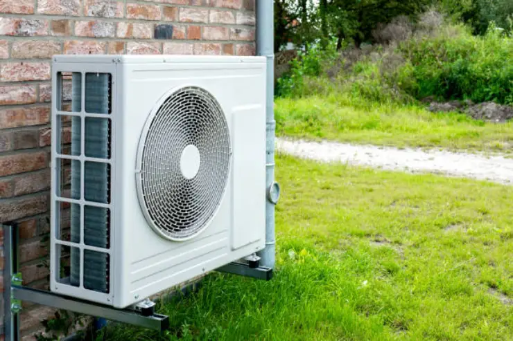 A single-fan air-source heat pump unit mounted on a brick wall.