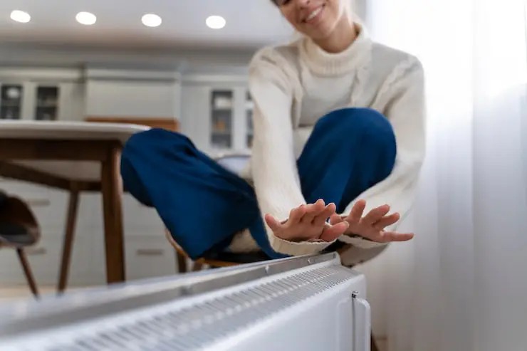 Woman warming hands over a home radiator or heat pump indoor unit.