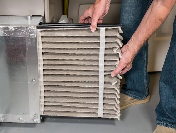 Removing a clogged air filter to improve furnace airflow.