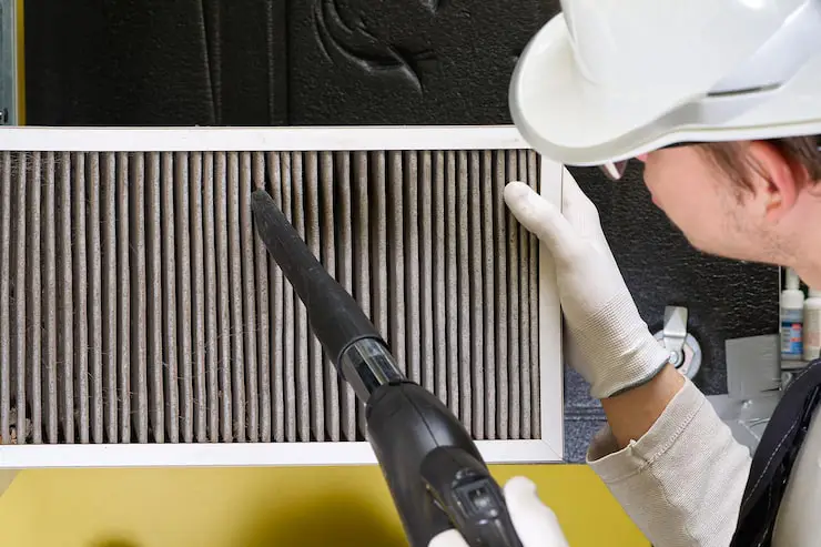 Technician vacuuming dust from a furnace air filter.
